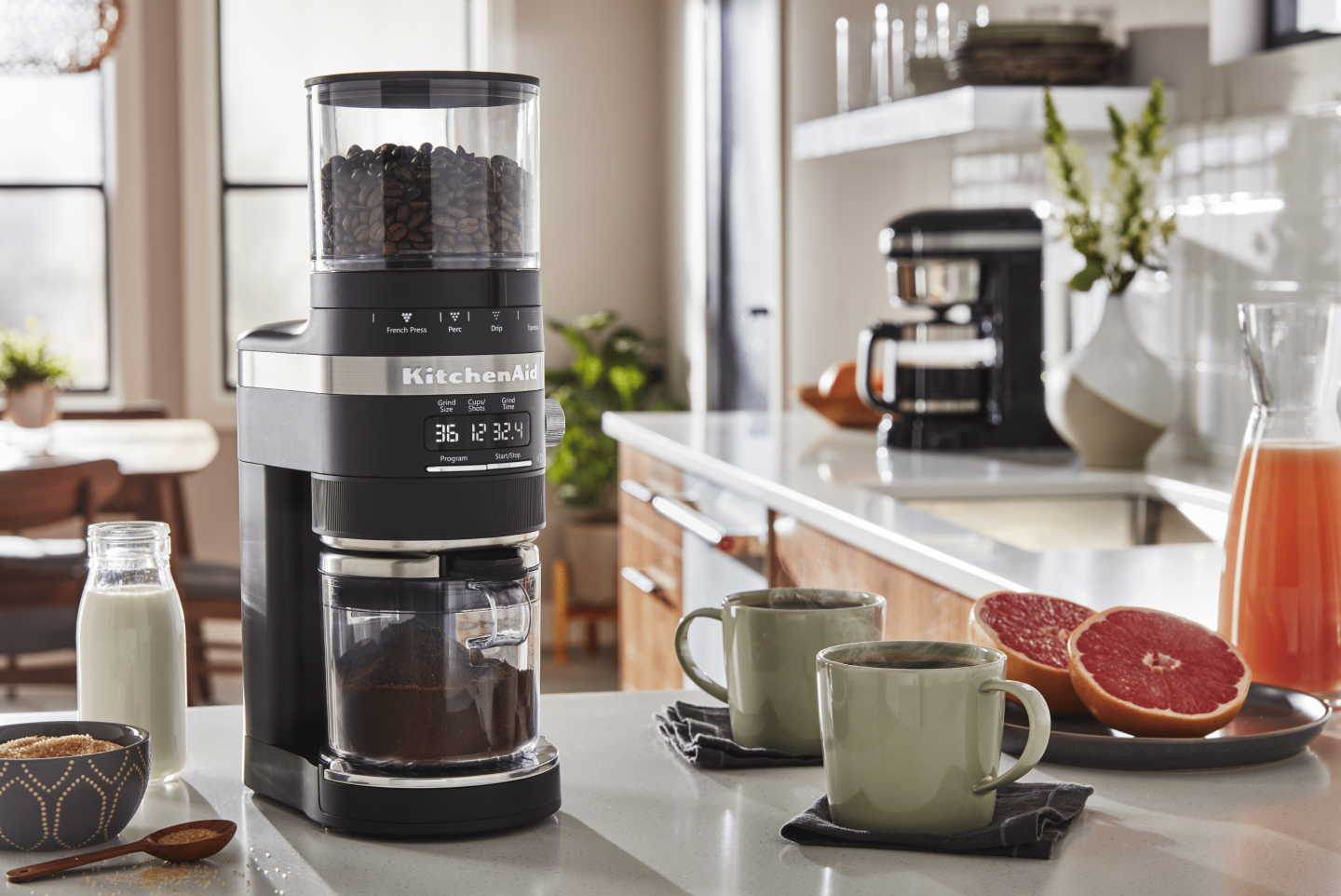 Same as Image Alt Text KitchenAid® burr grinder full of coffee beans next to two mugs